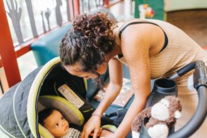 Woman playing with baby in stroller, stuffed monkey in one of the cup holders of the stroller.