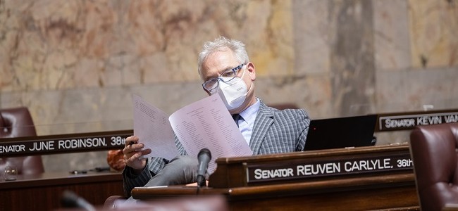 Senator Reuven Carlyle reads from paper while wearing a mask on the senate floor in olympia washington