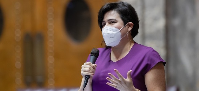 Senator Emily Randall holds a microphone while wearing an N95 mask and delivers a speech in the senate in olympia