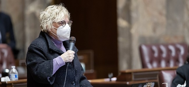 Senator Claire Wilson speaks into a microphone while wearing an N95 mask in the senate chambers in Olympia